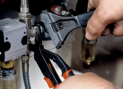 Hand using Ergo Big Mouth Adjustable Wrench With Rubber Grip 8 Inch For Tight Spots on plumbing pipe work under a sink.