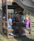 Children playing in cedar wood swing set with wave slide and elevated clubhouse play kitchen and picnic area.