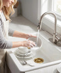 Woman washing dishes in sink with Golden Stainless Steel Garbage Disposal Flange And Sink Stopper For Three And One Half Inch Drain Hole Dope Frosted Gold Finish That Resists Discoloration Easy Install Kitchen Sink Accessory visible.