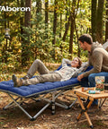 A couple enjoys camping with a Beefy 28 Inch Wide Camping Cot For Adults, Heavy Duty 1200D Oxford Fabric, in a forest setting.