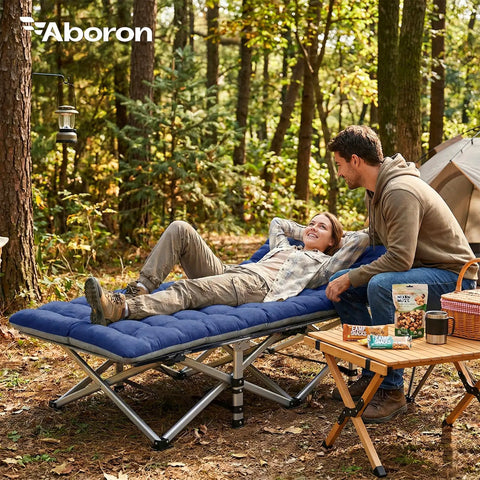 A couple enjoys camping with a Beefy 28 Inch Wide Camping Cot For Adults, Heavy Duty 1200D Oxford Fabric, in a forest setting.