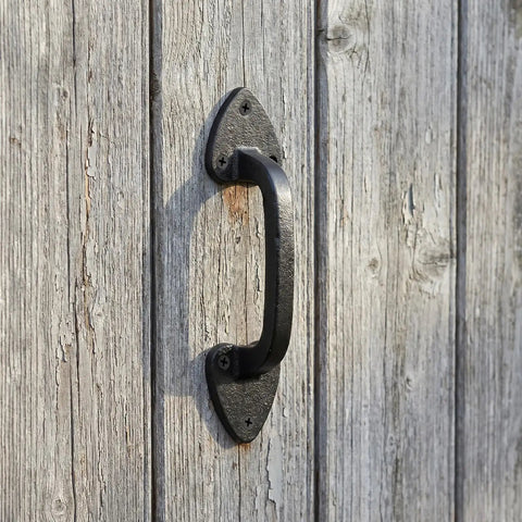 Close-up of heavy duty cast iron barn door handle in black aged finish on rustic wood, vintage industrial style.