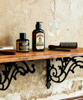 16 Inch Cast Iron Shelf Brackets 4 Pack Black Corbels Built Different Heavy Duty Wall Mounted Shelf Supports Up To One Hundred Pounds With Mounting Hardware holding grooming products on a wooden shelf.
