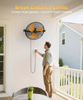 Man adjusting Heavy Duty 18 Inch Wall Mount Fan With Extended 6.6 Ft Cord, installed on a covered patio wall.