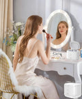 Woman using mirror in bedroom with Ultrasonic Retainer Cleaner 46kHz 2-in-1 Jewelry and Dental Cleaning Machine visible on table.
