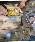 Front view of KICHOUSE stainless steel detacher tool beside a yellow tackle box with hooks and lures on a wooden table