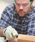 Man wearing dust blocking nose filter mask for woodworking with gloves and safety goggles, focusing on a piece of wood.