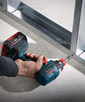 Side view of a Bosch cordless impact driver with blue body and red accents being used to drive a bit into metal framing.