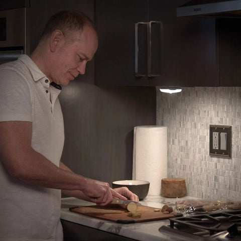 Man chopping vegetables under Battery Operated LED Puck Light For Under Cabinets And Shelves With Motion Sensor And Auto Shut Off After 20 Seconds 30 Lumen Bright White Cabinet Lighting No Fuss Easy Install