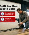 Man kneels on a wooden floor, applying black gaffer tape to secure cables.