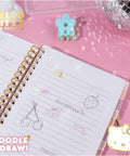 Hello Kitty Pink Gold Foil Journal Set For Girls with lined pages showing doodles, spiral binding, and tabs on pink background.