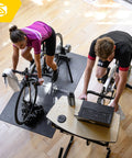 Two cyclists using Fluid2 Indoor Bike Trainer For Road And Mountain Bikes With Realistic Road Feel And Progressive Fluid Resistance