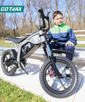 Off Road Electric Dirt Bike With 16 Inch Pneumatic Tires 300W Brushless Motor 15.5 MPH Top Speed 16 Mile Range Dual Suspension And Disc Brake Trail Ready Ride For 47 To 67 Inches Black showcased near bleachers outdoors with a young rider sitting beside.