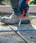 QLT Pull Tie Wire Twister for concrete and rebar tying, being used by a worker wearing gloves, 12-inch rubber grip handle.