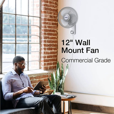 Commercial Grade Oscillating Wall Mount Fan, 12 Inch White, installed on a brick wall in an office setting, 3-Speed 120V motor.