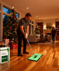 Person using All-In-One Golf Hitting Mats Trainer For Driving, Chipping And Putting indoors with Christmas decorations
