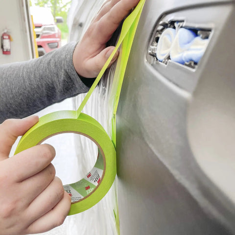 Applying Pro Grade Performance Masking Tape 233 Plus, 24 mm Wide By 55 M Long, to a car surface for precise auto body painting.