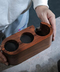 Person holding 58mm Espresso Tamper Station With Rosewood Finish All In One Coffee Bar Organizer, showing slots for tools.