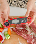 Person holding Instant Read Meat Thermometer With Magnetic Back And Bottle Opener over raw steak and vegetables