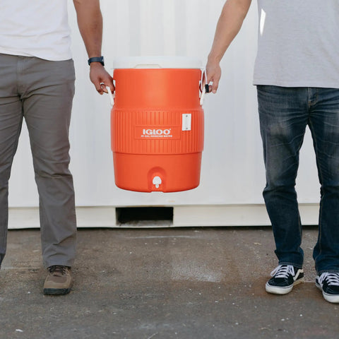 10 Gallon Portable Sports Cooler And Beverage Dispenser With Flat Seat Lid Insulated For All Day On The Go Chillin, carried by two people.