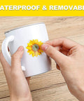 Applying a sunflower decal from the 39 Piece 3D Sunflowers And Butterflies Wall Decals Set With Gold Accents to a mug