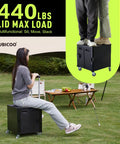 Foldable Rolling Utility Cart With Lid On Wheels Collapsible Handcart Trolley For Grocery Shopping Office Camp School And File Organization Durable Black With Brakes And Large Capacity being used as a seat and step stool outdoors.
