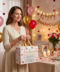 Woman holding Anniversary Gift Bag For Hubby With Greeting Card And 3 Tissue Paper Romantic Heart Theme Wrap Bag For Men in decorated room.
