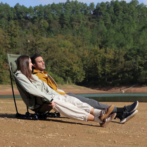 Two people sitting on a Compact High Back Camp Chair With Dual Sitting Modes Pillow Arm Pads And Side Pockets by a lake