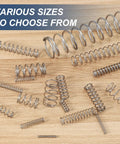 Various sizes of 304 stainless steel springs on a wooden surface, including DIY Friendly Compression Spring 12 Mm Outer Diameter 1 Mm Wire 25 Mm Free Length 304 Stainless Steel Small Extension Spring Pack Of 10 For Home Projects Repairs And Electronics Tools