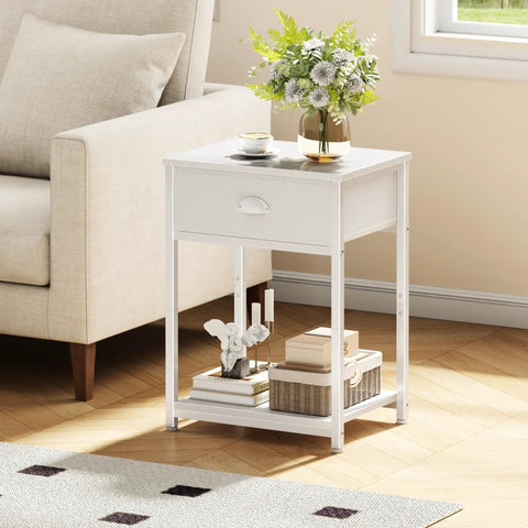 Small Space Friendly White Nightstand With Fabric Drawer And 3 Tier Storage End Table For Living Room Bedroom Or Dorm Durable Night Stand With Adjustable Feet Sturdy Build For Daily Use beside sofa, featuring plants and decor items on top, books and storage on lower shelves.