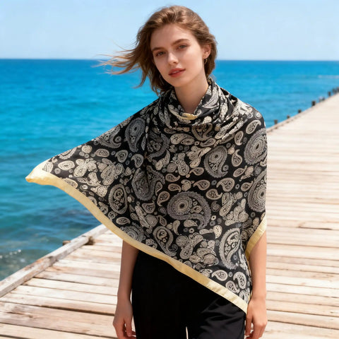 43 Inch Square Silk Feeling Scarf For Hair And Neck Wrap worn as a shawl, lightweight satin polyester blend, 110cm by 110cm, on a boardwalk.