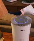 Premium Hepa Air Purifier With H13 True Filters And Uv Light Plus Activated Carbon on a table beside a lamp.