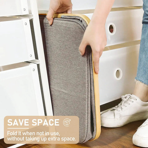 Gray Collapsible Laundry Basket 105L Tall Foldable With Bamboo Handle being stored easily under a dresser in a bedroom.