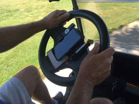 Golf Cart Steering Wheel Phone Mount Pro With Spring Loaded Arms And Scorecard Holder Fits Any Phone Two To Three Point Five Inches Easy On Off Made In USA Rotates Up And Down For Convenient Scorekeeping holding a phone and scorecard on a steering wheel.