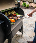 Person grilling vegetables and steaks on a Wood Pellet Grill And Smoker That Delivers Wood Fired Flavor With Big 884 Square Inches Cook Area