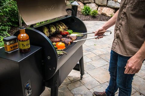 Person grilling vegetables and steaks on a Wood Pellet Grill And Smoker That Delivers Wood Fired Flavor With Big 884 Square Inches Cook Area