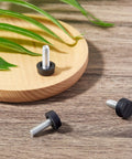 Forty Piece Heavy Duty M6 Thread Adjustable Furniture Levelers And Screw In Feet To Squash Wobbly Tables And Chairs Quick With Grip Tight Glides That Stop The Wobble Forever For Indoor Or Outdoor Setup close-up of three black levelers on wood surface.