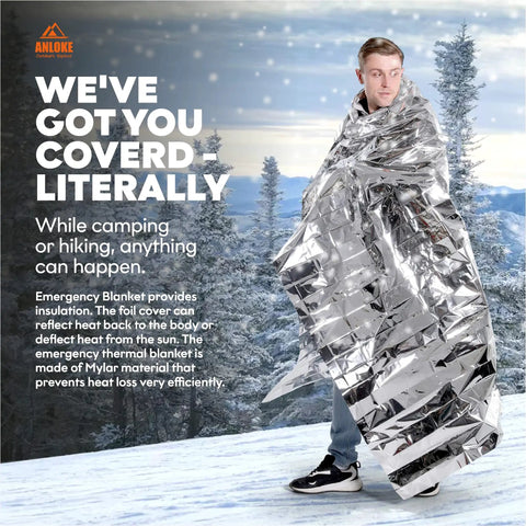 Person wrapped in Emergency Mylar Thermal Blanket from 10 Pack, standing in snowy forest. Giant space blankets 84x64 inches for survival.