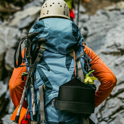 Hiker with backpack and Nonstick Camping Cookware Mess Kit with lightweight pot and fry pan mesh bag included for outdoor cooking.