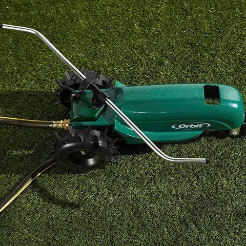 Traveling sprinkler system on grass showing tractor wheel, gear housing, and sprinkler arms in silver and green finish.