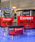 Front view of Expert Reinforced Metal Filler With Aluminum Reinforcement For Built Tough High Strength And Heat Resistant Auto Repairs Durable Automotive Repair Filler 237 Milliliters, along with other body fillers on a table.