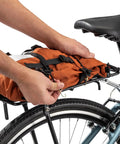 Person attaching orange bag to Rear Bike Rack For Everyday Hauls Lightweight Durable Cargo Carrier With 26 Lb Capacity That Fits Most Adult Bikes.