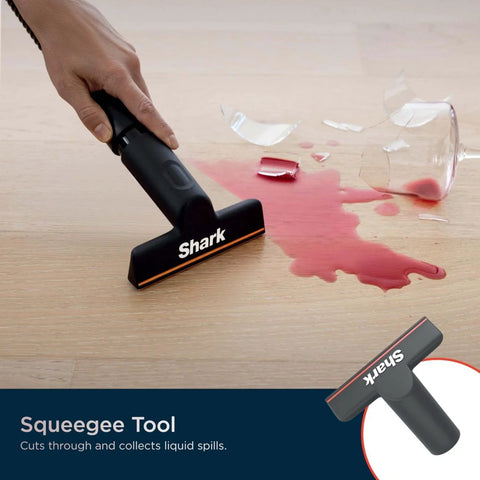 Hand using Shark squeegee tool to clean spilled liquid from a broken glass on a wooden floor.