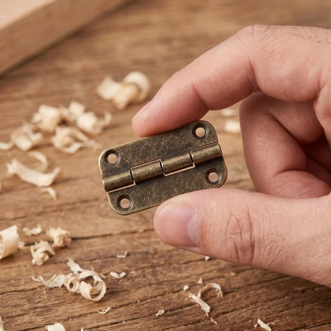 Hand holding a 12 Pack Small Iron Hinges with rounded corners, 1.4 inch antique bronze cabinet butt hinge for wooden jewelry boxes.