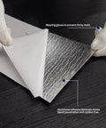 Hands peeling back a layer of Peel And Stick Vinyl Floor Tiles Wood Plank Look Black Finish 24 Sheets Covering 36 Sq Ft No Mess DIY Friendly Waterproof Scratch Resistant Super Easy Install With Heavy Duty Adhesive And Sound Insulation to reveal aluminum adhesive laminate.