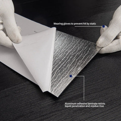 Hands peeling back a layer of Peel And Stick Vinyl Floor Tiles Wood Plank Look Black Finish 24 Sheets Covering 36 Sq Ft No Mess DIY Friendly Waterproof Scratch Resistant Super Easy Install With Heavy Duty Adhesive And Sound Insulation to reveal aluminum adhesive laminate.