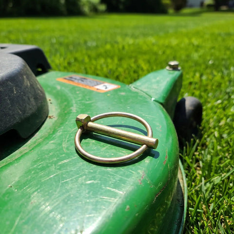 Get Your Yard Gear Fixin' With These 12 Heavy Duty Carbon Steel Retaining Pins Featuring Ring Locks For Tractors Mowers And Trailers To Keep Everything Secure And Rust-Free In The Dirt, showcasing a retaining pin on a green mower.