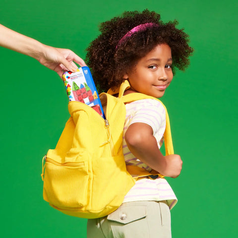 Child placing a Travel Magnetic Construction Set With 26 MicroMAGS Tiles into a yellow backpack