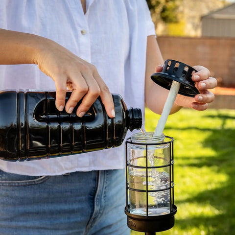 Person pouring Mosquito Repellent Torch Fuel Duo Pack 100 Oz Citronella Cedar Formula For Outdoor Mosquito Control into a torch