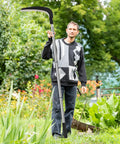 Person holding Beast Scythe Tool For Grass Cutting And Weeding Sickle Garden Tool with adjustable long handle in a garden.